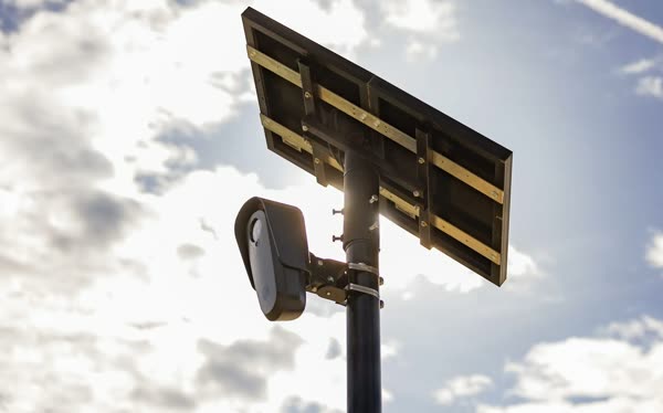 A Flock Safety license plate camera and its solar panel on a pole against a cloudy sky